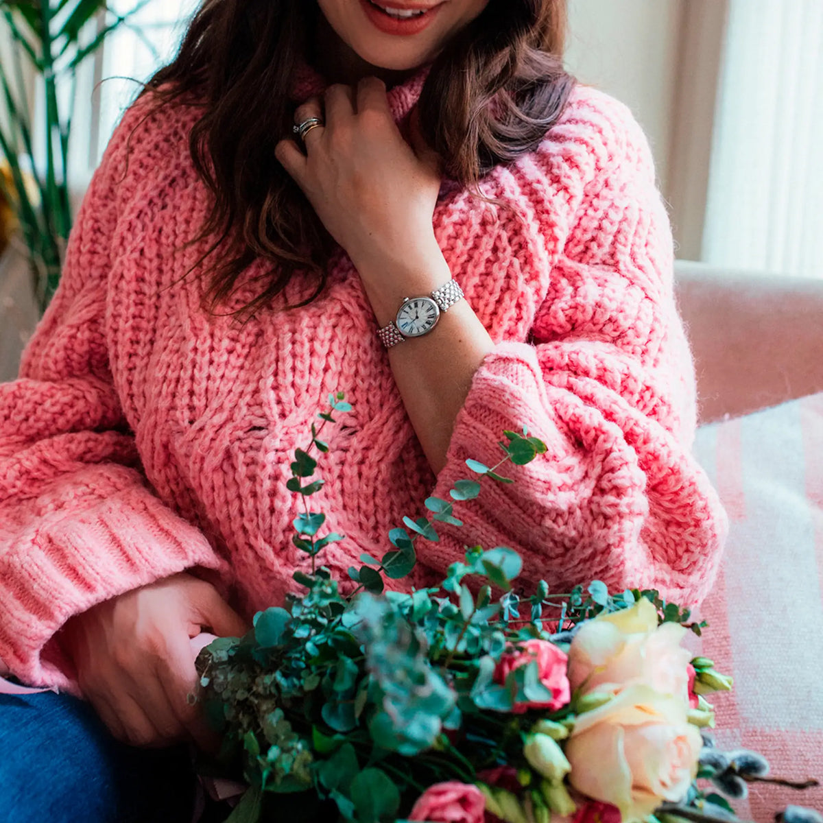 Frau in einem pink-rosanen Stickpullover mit einem Blumenstrauß in der Hand trägt die Art Deco Oval von Frederique Constant an ihrem Handgelenk