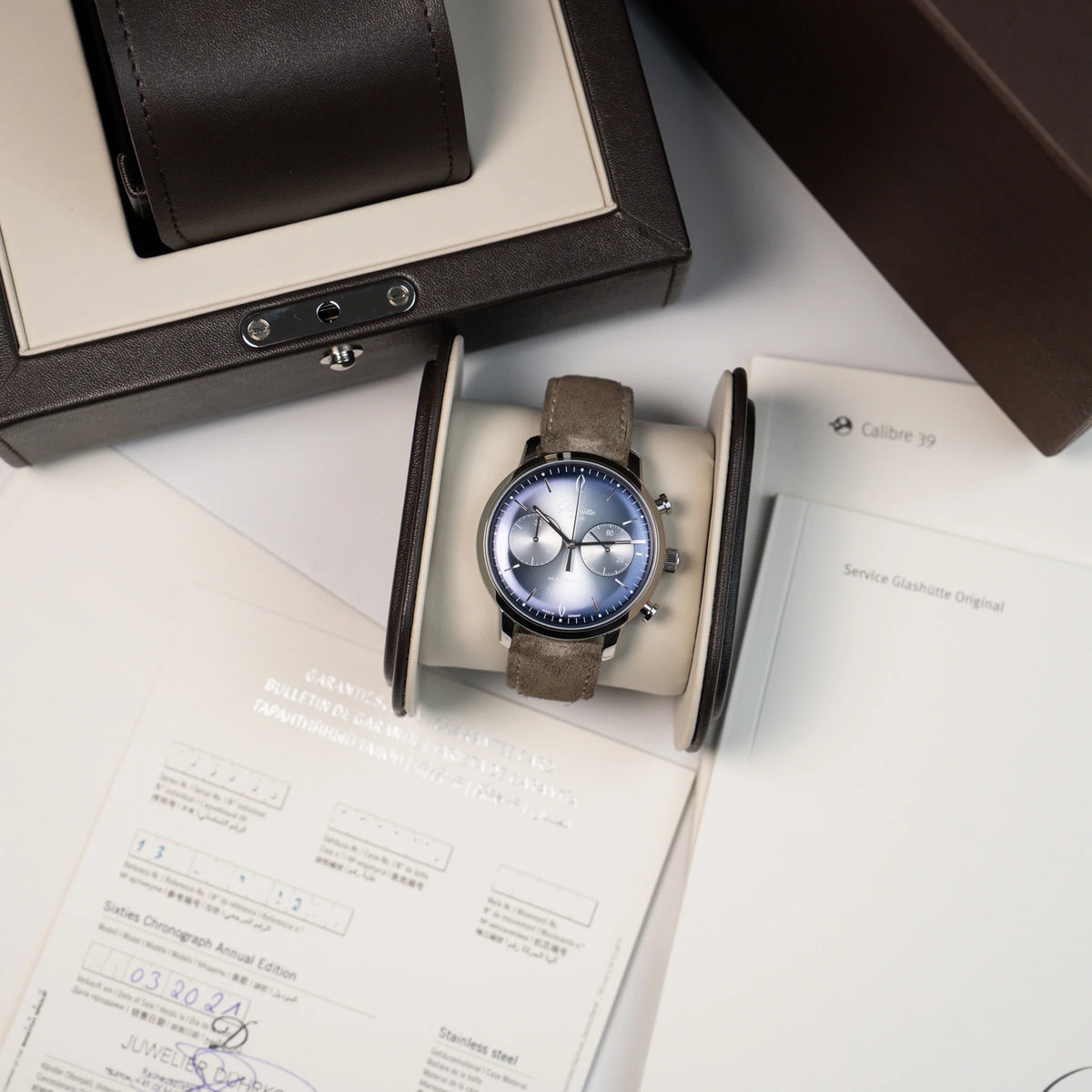 Produktfotografie der Glashütte Original Sixties Chronograph mit blauem Sonnenschliff-Zifferblatt zusammen mit dem Lieferumfang