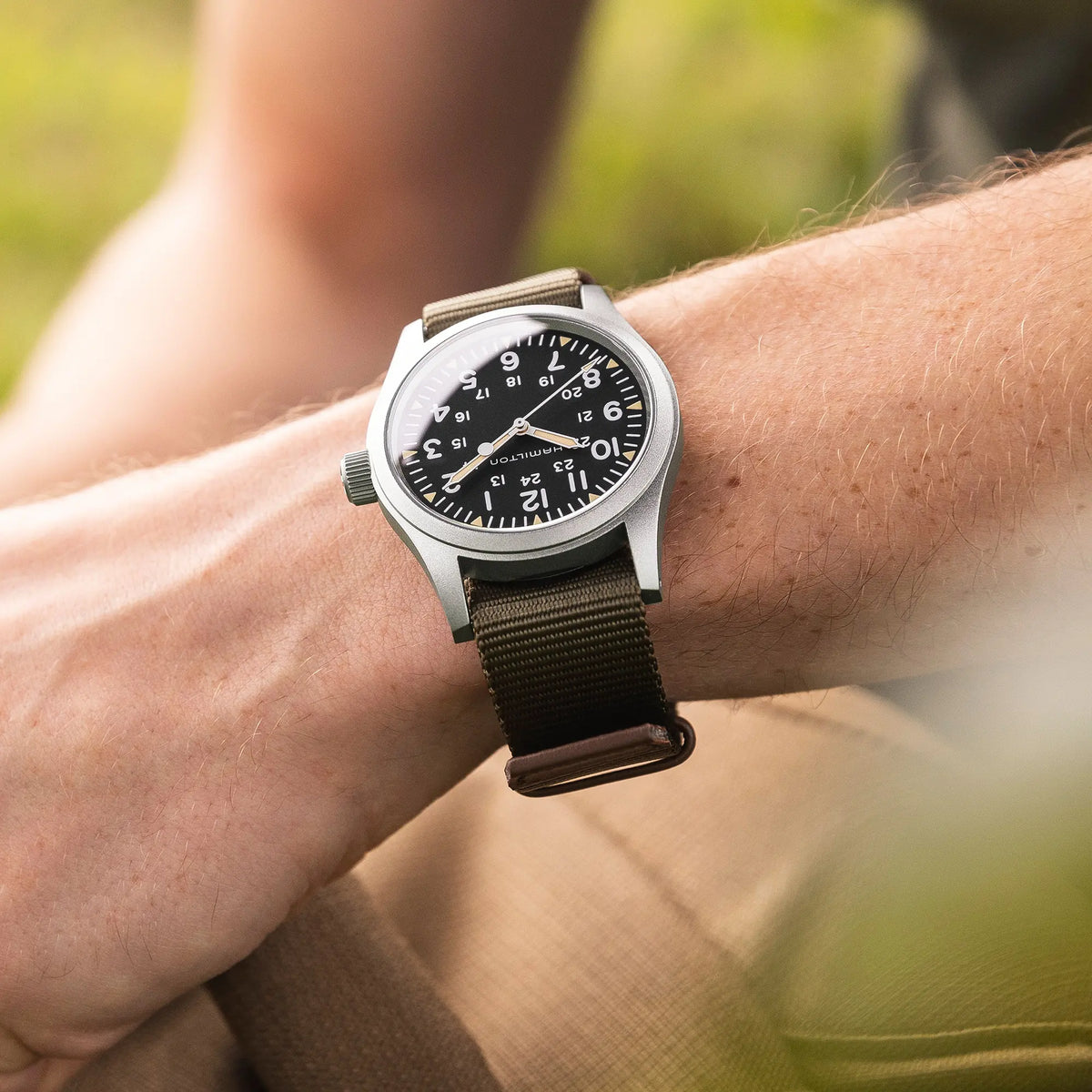 Mann trägt die Hamilton Khaki Field Mechanical H69439931 mit weißem Zifferblatt an einem olivgrünem Nato-Textil-Armband an seinem Handgelenk