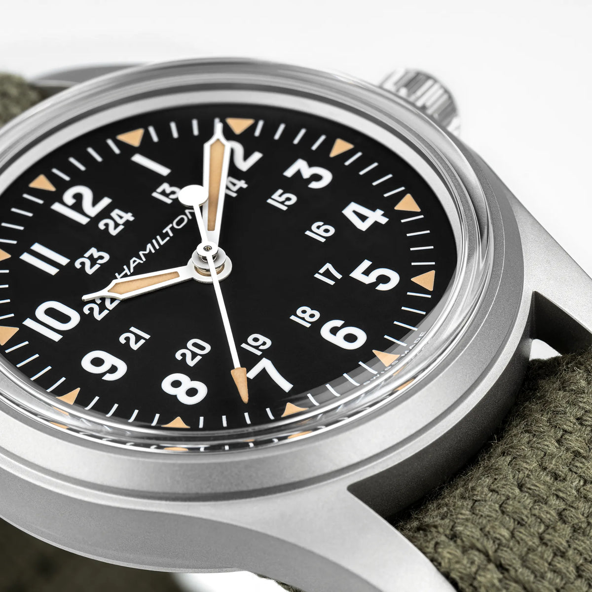 Detailansicht der Hamilton Khaki Field Mechanical H69399930 mit schwarzem Zifferblatt im Vintage-Charakter mit Indizes in weiß und beige an einem khaki-farbenem Nato-Band zeigt das Acrylglas