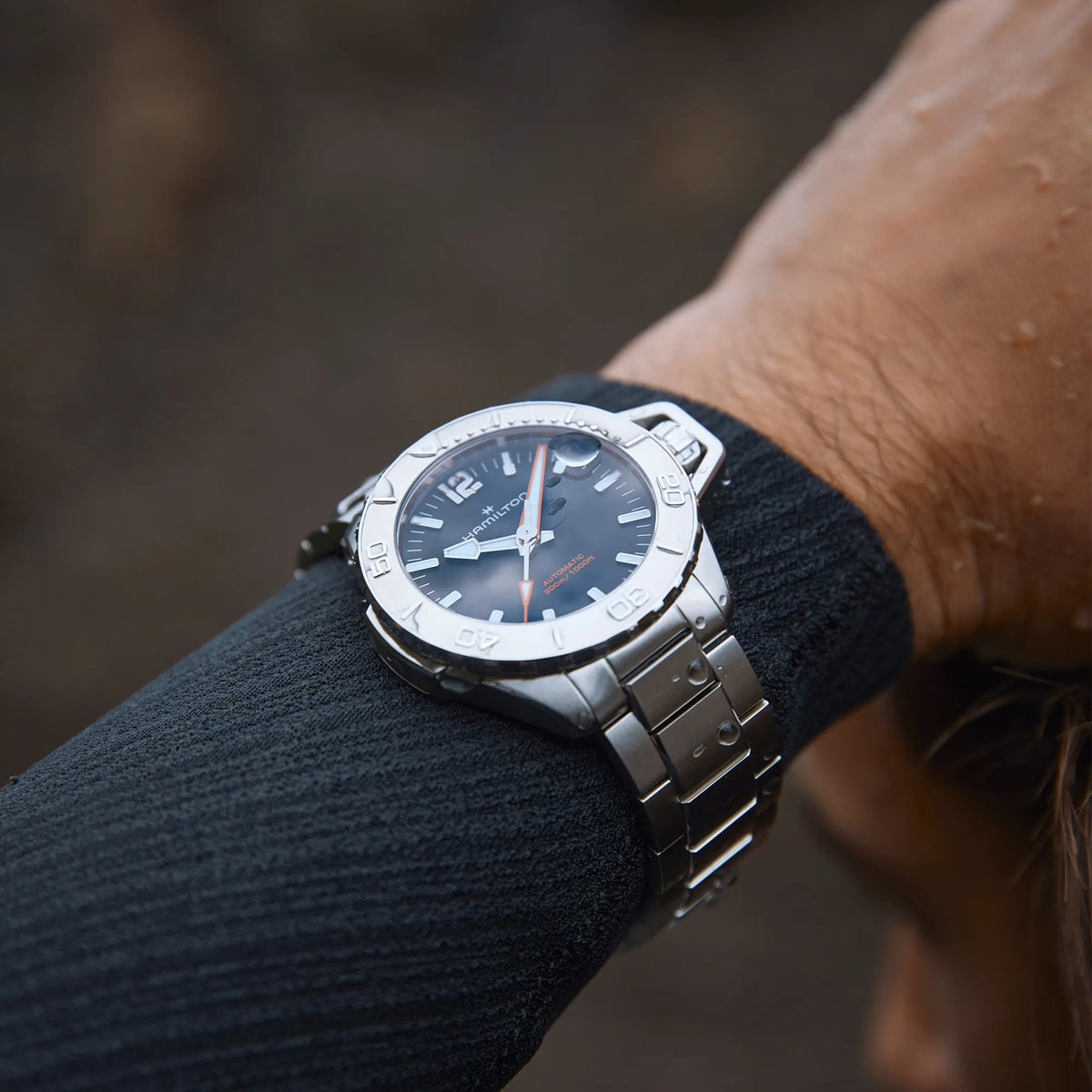 Blick auf das Handgelenk eines Mannes im Neoprenanzug, der darüber eine Hamilton Taucheruhr trägt