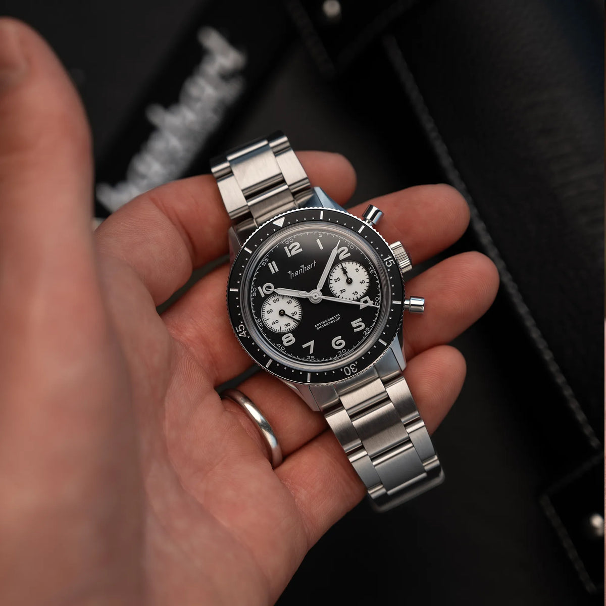 Mann hält die Hanhart 415 ES Chronographs mit dem Reverse-Panda-Zifferblatt in Schwarz mit weißen Sub-Dials am Edelstahlarmband und präsentiert die Uhr in die Kamera