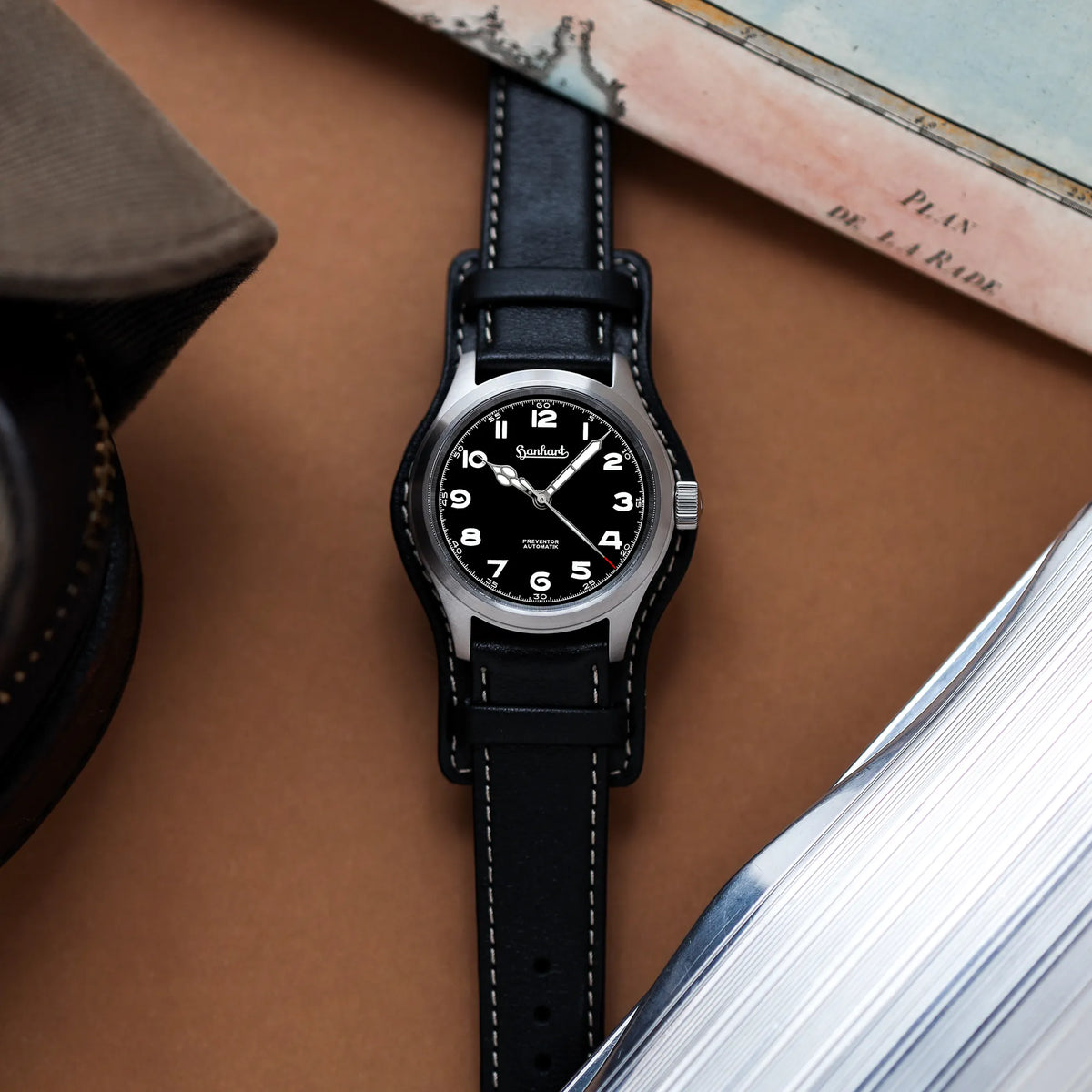 Produktfotografie der Hanhart Preventor HD12  Dreizeiger-Uhr mit schwarzem Zifferblatt am schwarzen Lederband mit Lederunterlage