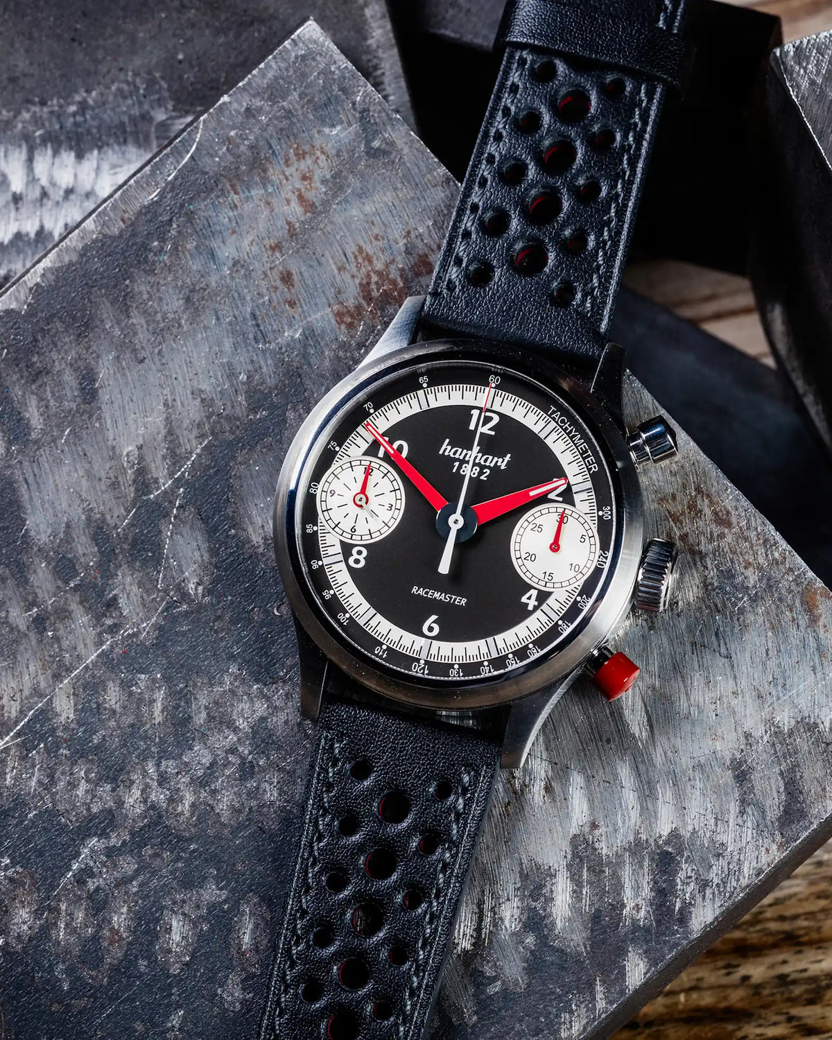Produktfotografie der Hanhart Pioneer Racemaster mit roten Zeigern, während die Uhr auf einer Eisenplatte liegt