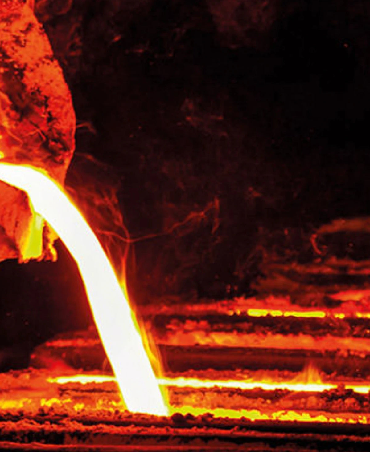 Fotografie in einer Metallgieserei mit orange glühendem Material, das gerade gegossen wird