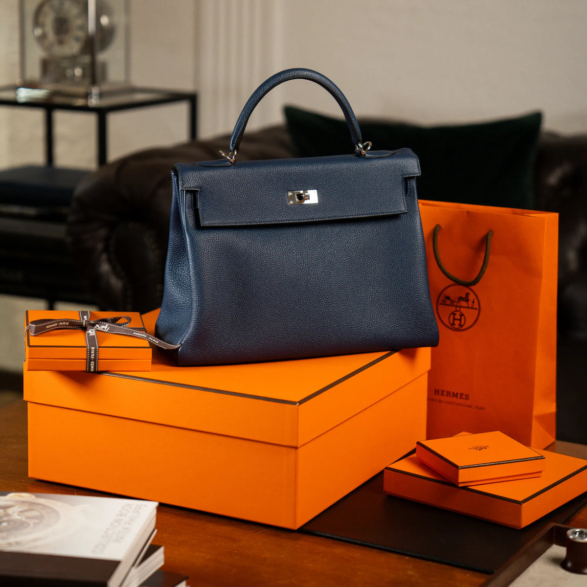 Produktfotografie der Hermes Kelly Bag 32 aus Togo-Kalbsleder in der Farbe Bleu-de-Prusse mit silberner Hardware, während die Tasche auf dem orangenem  Hermes Karton