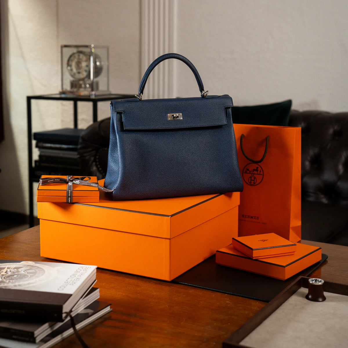 Produktfotografie der Hermes Kelly Bag 32 aus Togo-Kalbsleder in der Farbe Bleu-de-Prusse mit silberner Hardware zusammen mit den orangen Hermes-Kartons