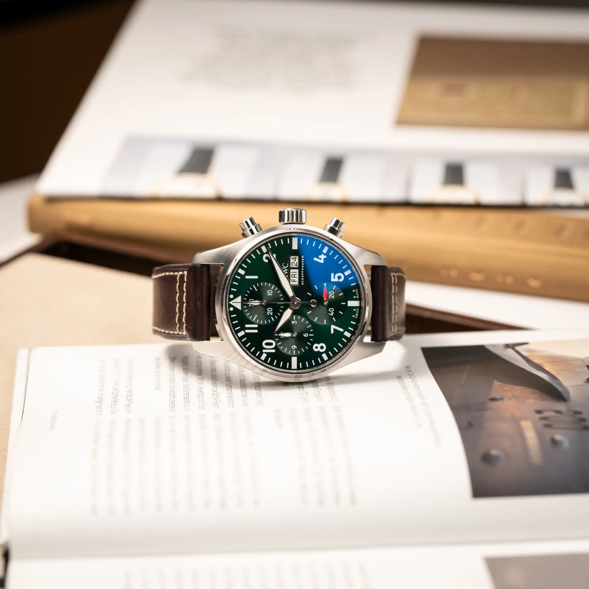 Produktfotografie des IWC Pilot 41 Chronographs IW388103 mit grünem Zifferblatt an einem braunen Lederband, während die Uhr auf der seitlichen Gehäuseflanke liegt
