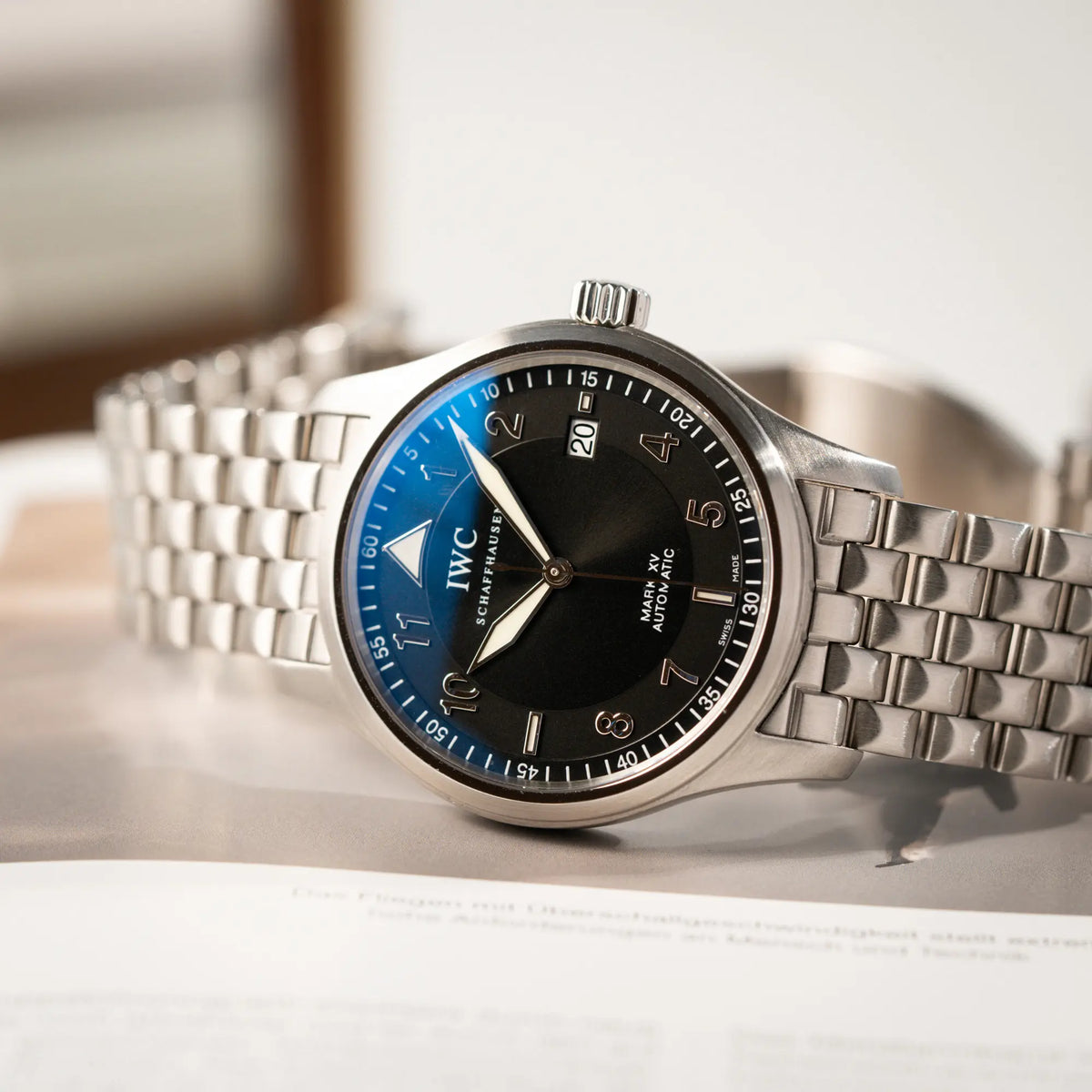 IWC Pilot Fliegeruhr Mark 15 der Referenz IW325312 aus 2005 mit dem schwarzen Zifferblatt an dem passenden, originalen 5-gliedrigen Stahlband liegt seitlich auf dem Uhrengehäuse