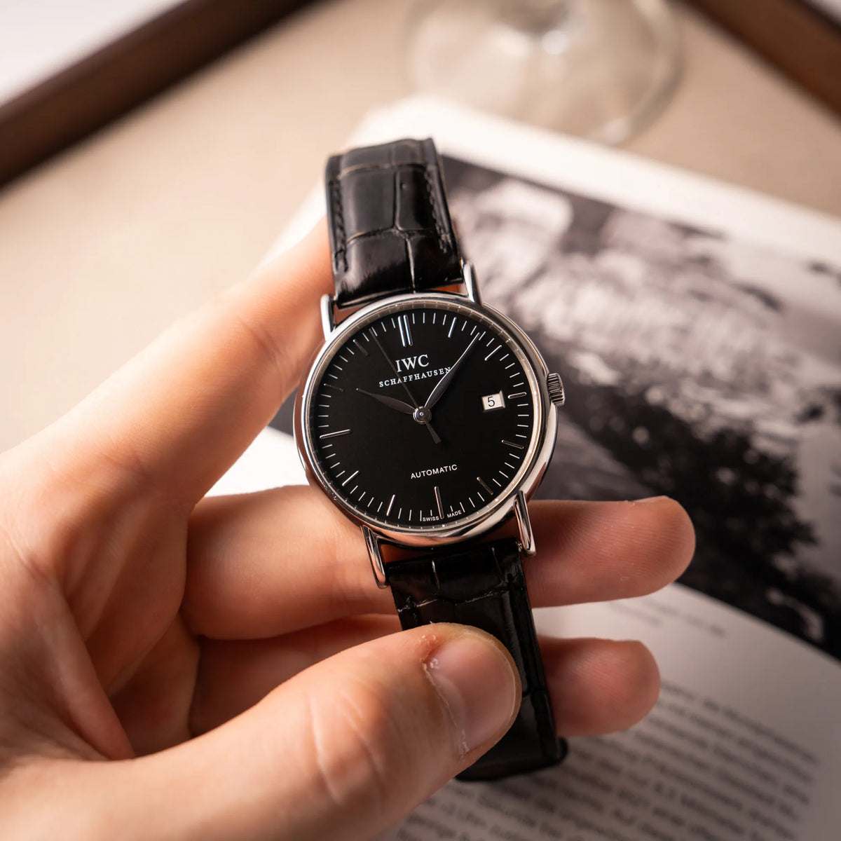 Mann hält die IWC Portofino Automatik IW356305 Armbanduhr mit minimalistischen, schwarzem Zifferblatt mit Stichindizes am schwarzen Lederband in der Hand und präsentiert die Uhr in die Kamera