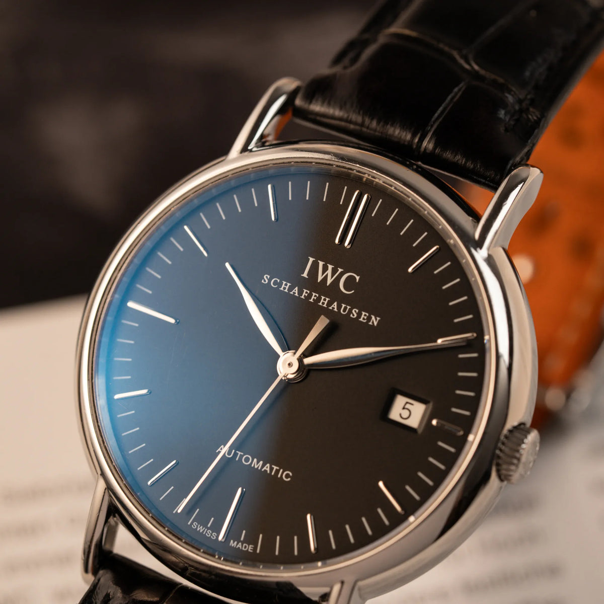 Detailaufname mit Fokus auf dem Zeigersatz der IWC Portofino Automatik IW356305 Armbanduhr mit minimalistischen, schwarzem Zifferblatt mit Stichindizes am schwarzen Lederband