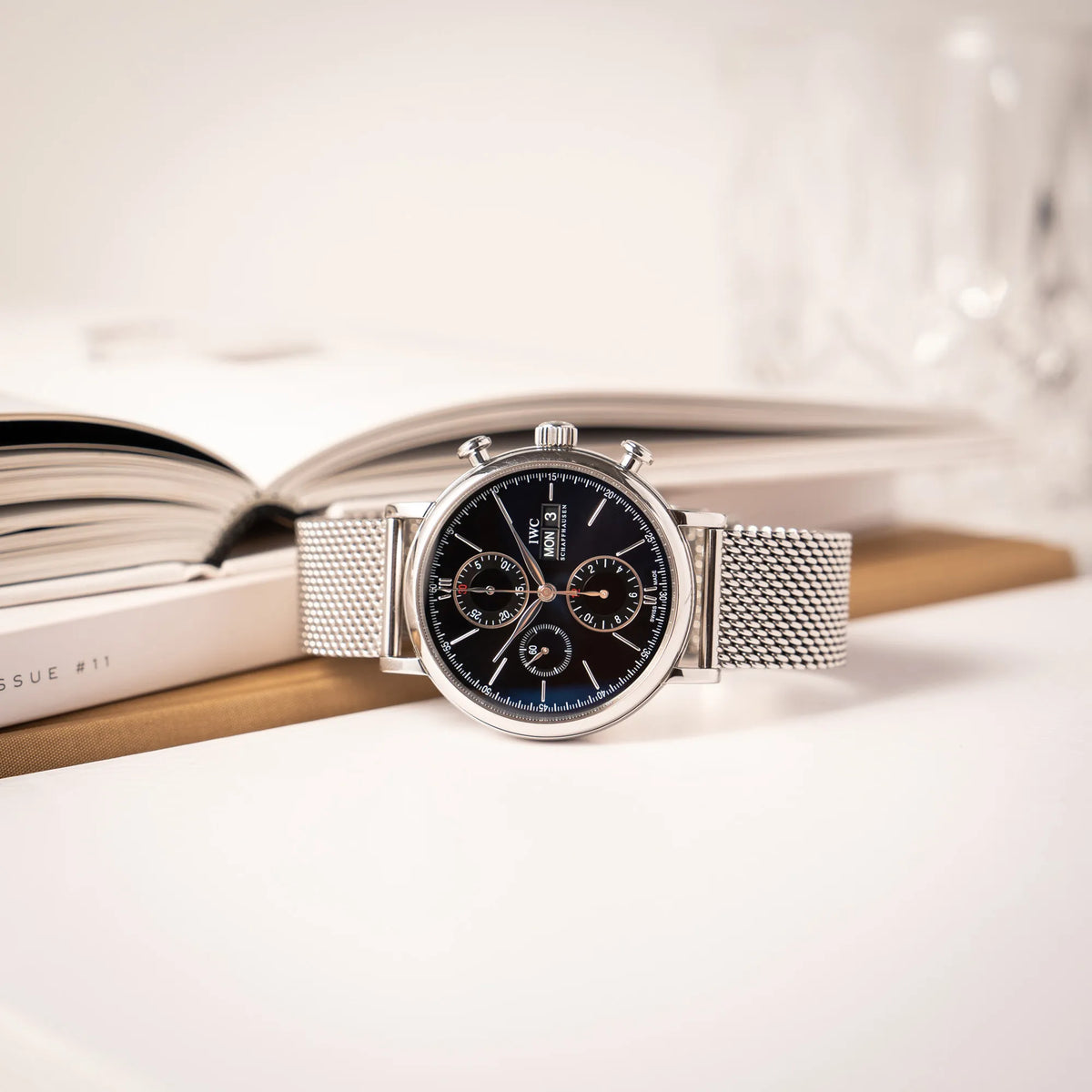 IWC Portofino Chronograph der Referenz IW391002 mit schwarzem Zifferblatt an einem Mesh-Armband lgt vor einem Stapel Büchere