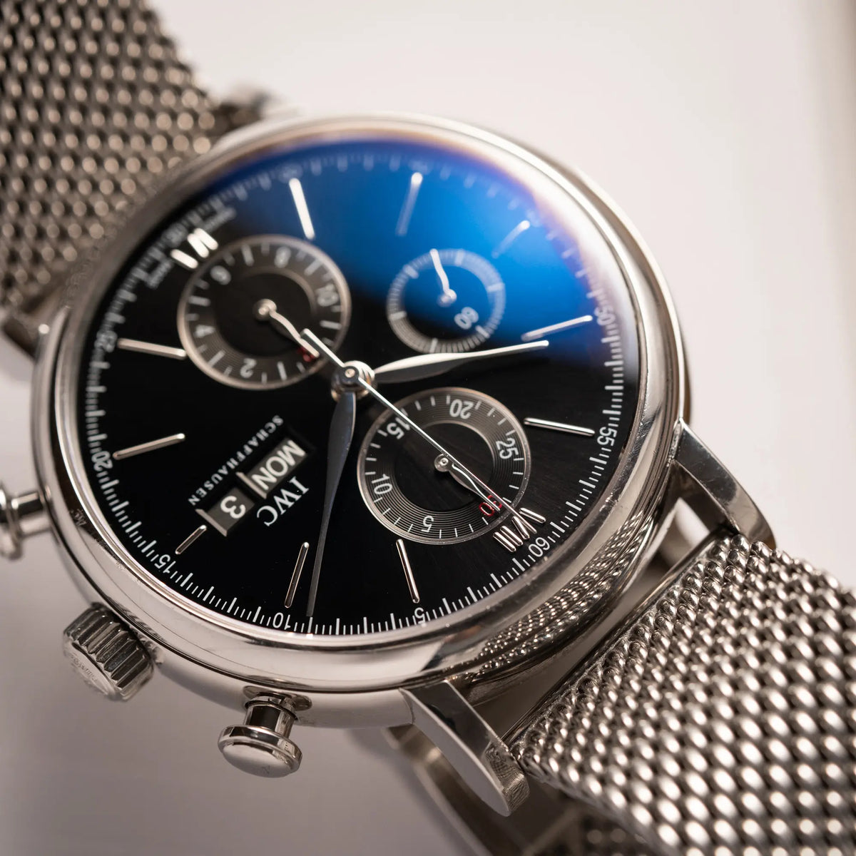 Detailaufnahme der IWC Portofino Chronograph der Referenz IW391002 mit schwarzem Zifferblatt an einem Mesh-Armband mit Blick auf die Chronograph-Drücker