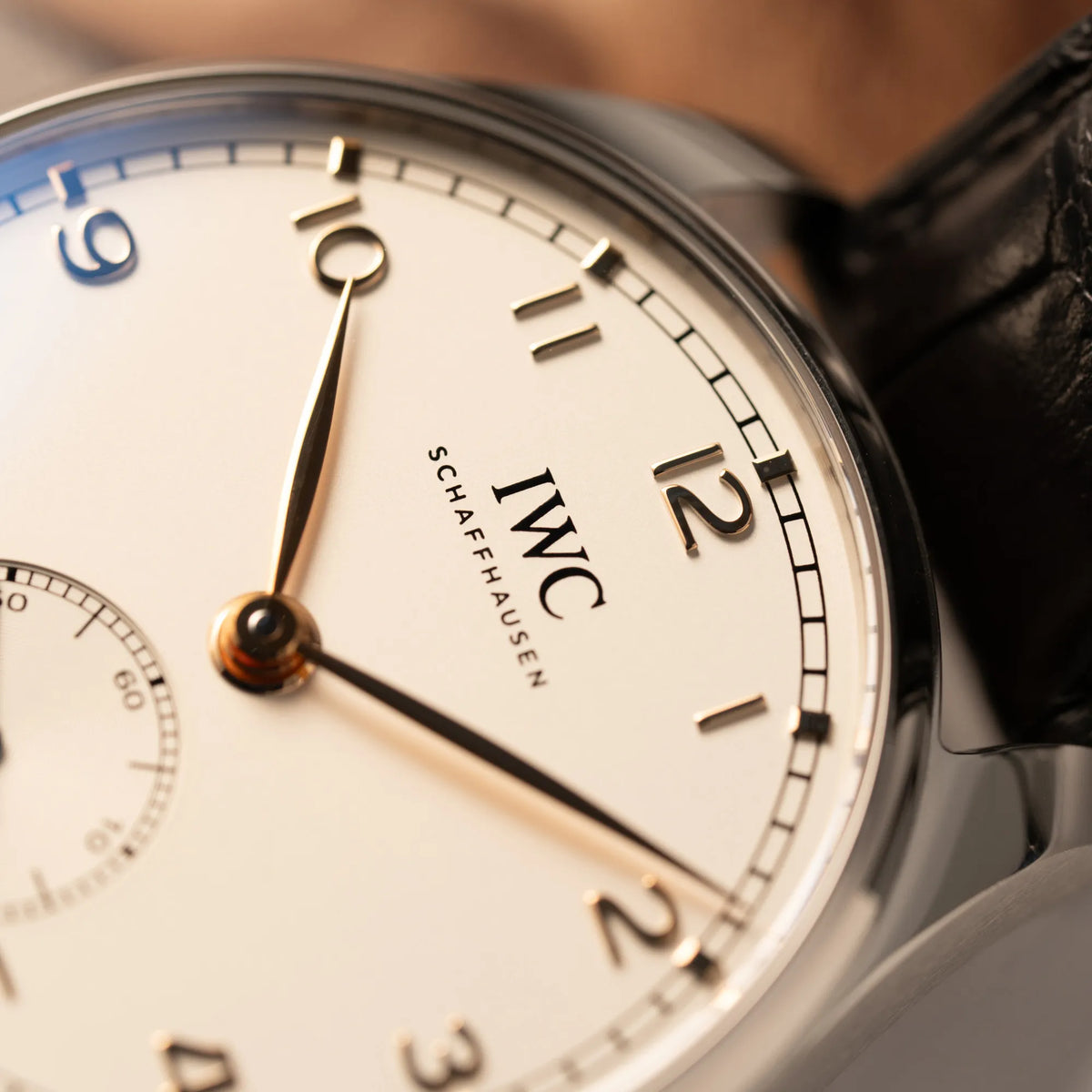 Detailaufnahme der IWC Portugieser 40 Automatik IW358303 mit weißem Zifferblatt und roségoldenen Zeiger- und Index-Details am schwarzen Lederband