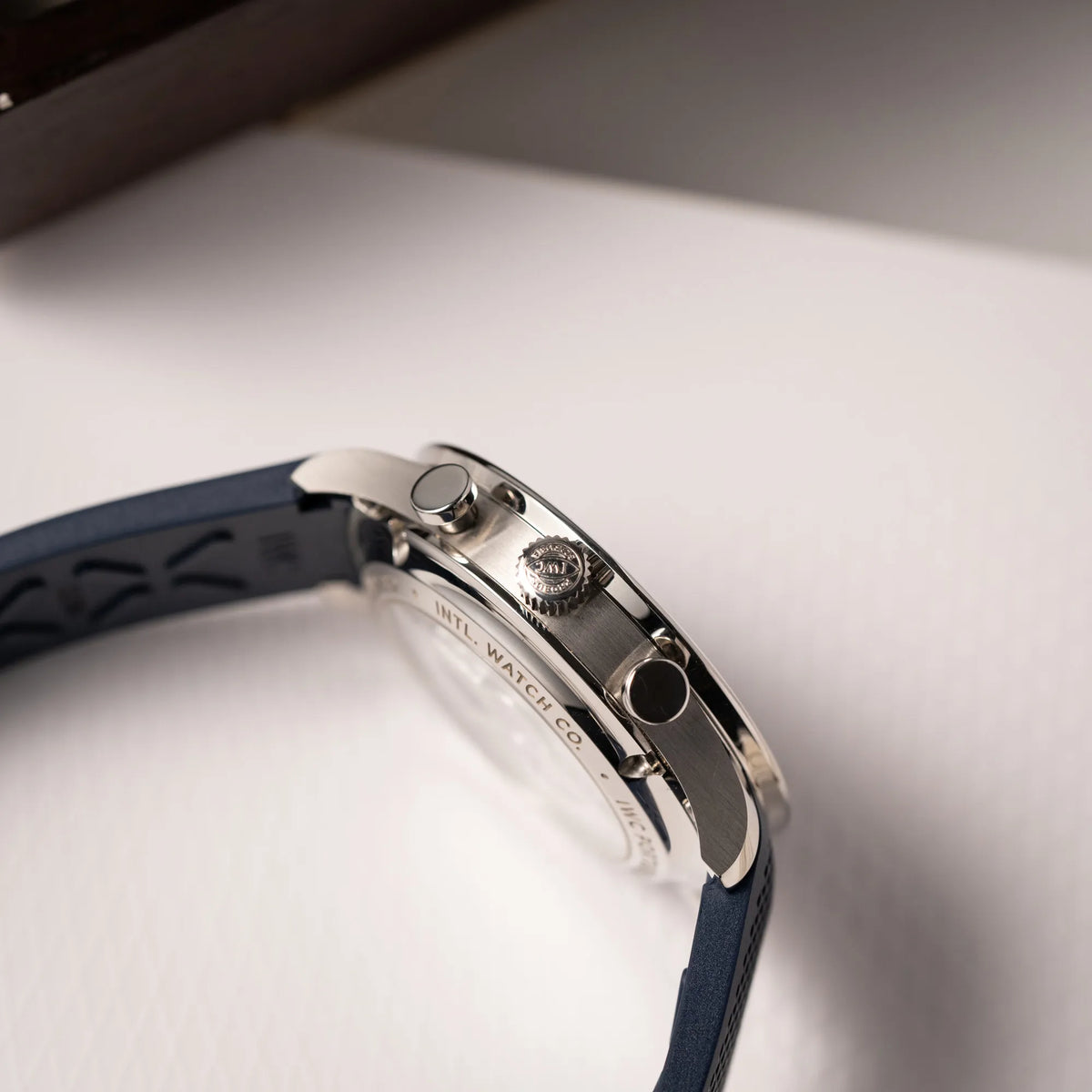 Seitliche Gehäuseflanke der IWC Portugieser Chronograph 41 der Referenz IW371620 mit weißem Zifferblatt und dunkelblauen Totalisatoren am passenden dunkelblauen Kautschukarmband mit Blick auf die Aufzugskrone und die Chronograph-Pusher