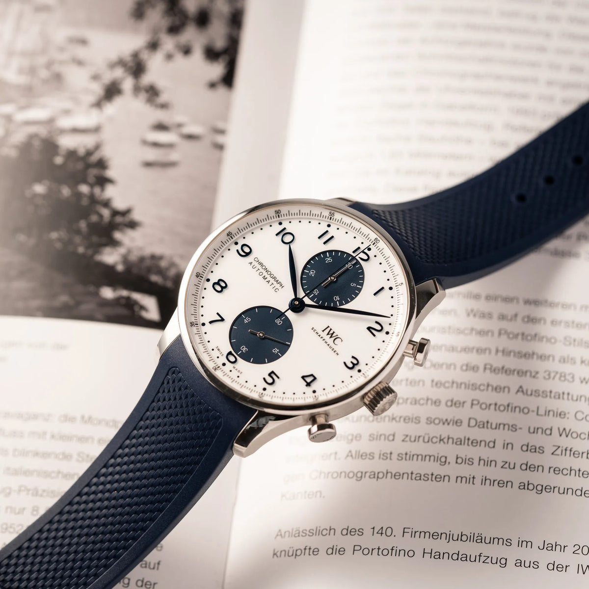 IWC Portugieser Chronograph 41 der Referenz IW371620 mit weißem Zifferblatt und dunkelblauen Totalisatoren am passenden dunkelblauen Kautschukarmband "steht" bei dieser Produktfotografie auf dem Kautschukarmband