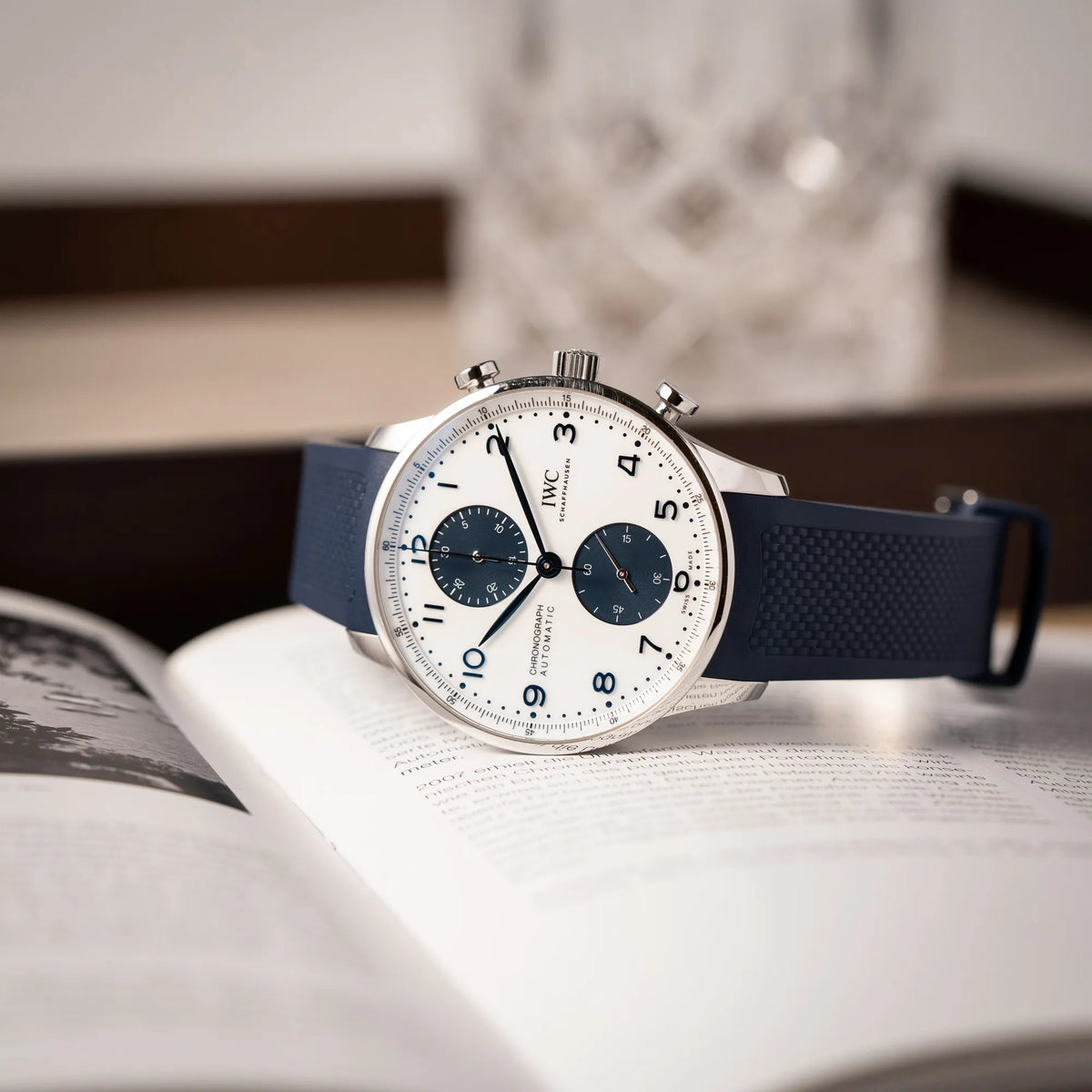 Produktfotografie der seitlich auf dem Uhrengehäuse liegenden IWC Portugieser Chronograph 41 der Referenz IW371620 mit weißem Zifferblatt und dunkelblauen Totalisatoren am passenden dunkelblauen Kautschukarmband