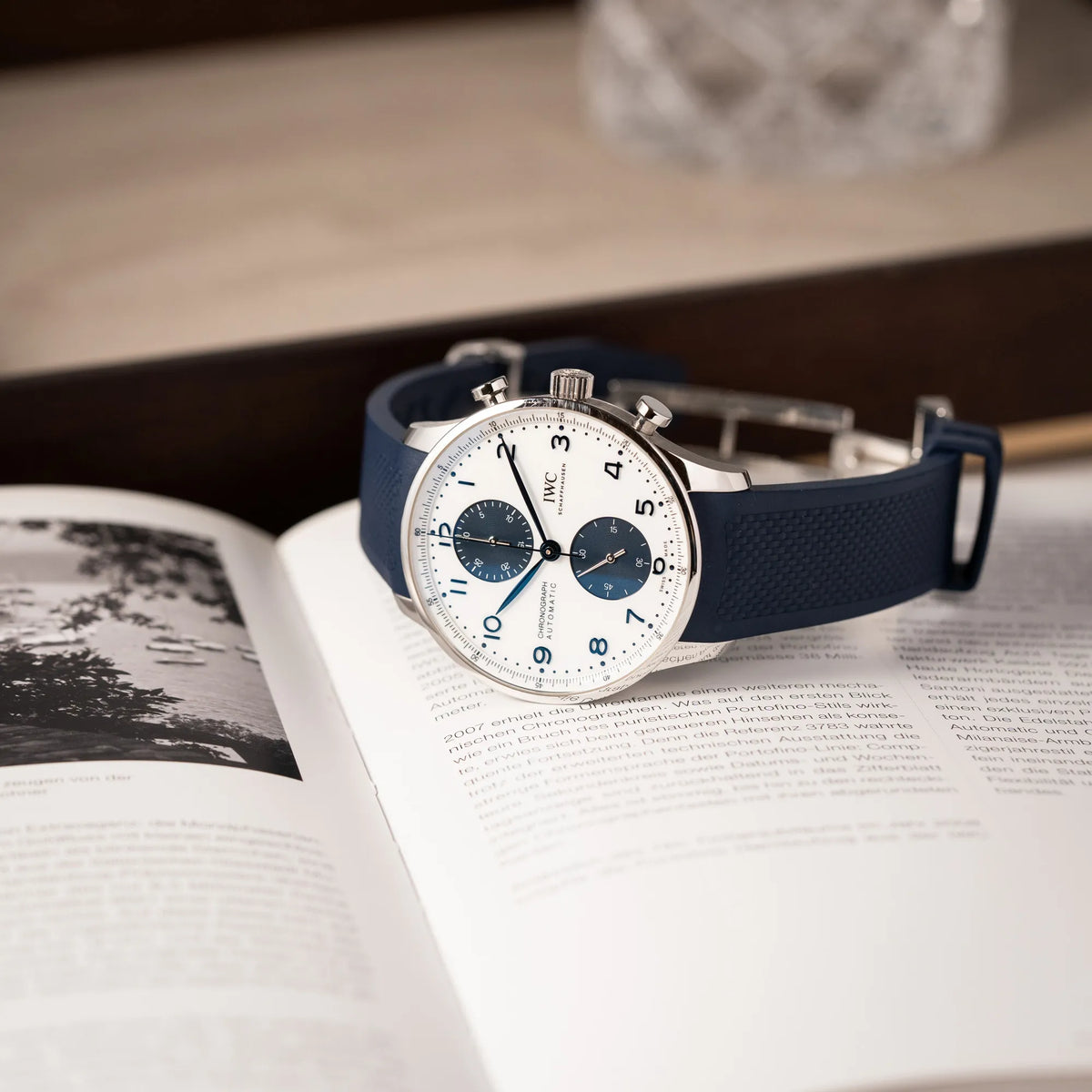 IWC Portugieser Chronograph 41 der Referenz IW371620 mit weißem Zifferblatt und dunkelblauen Totalisatoren am passenden dunkelblauen Kautschukarmband liegt auf einem Buch über Uhren