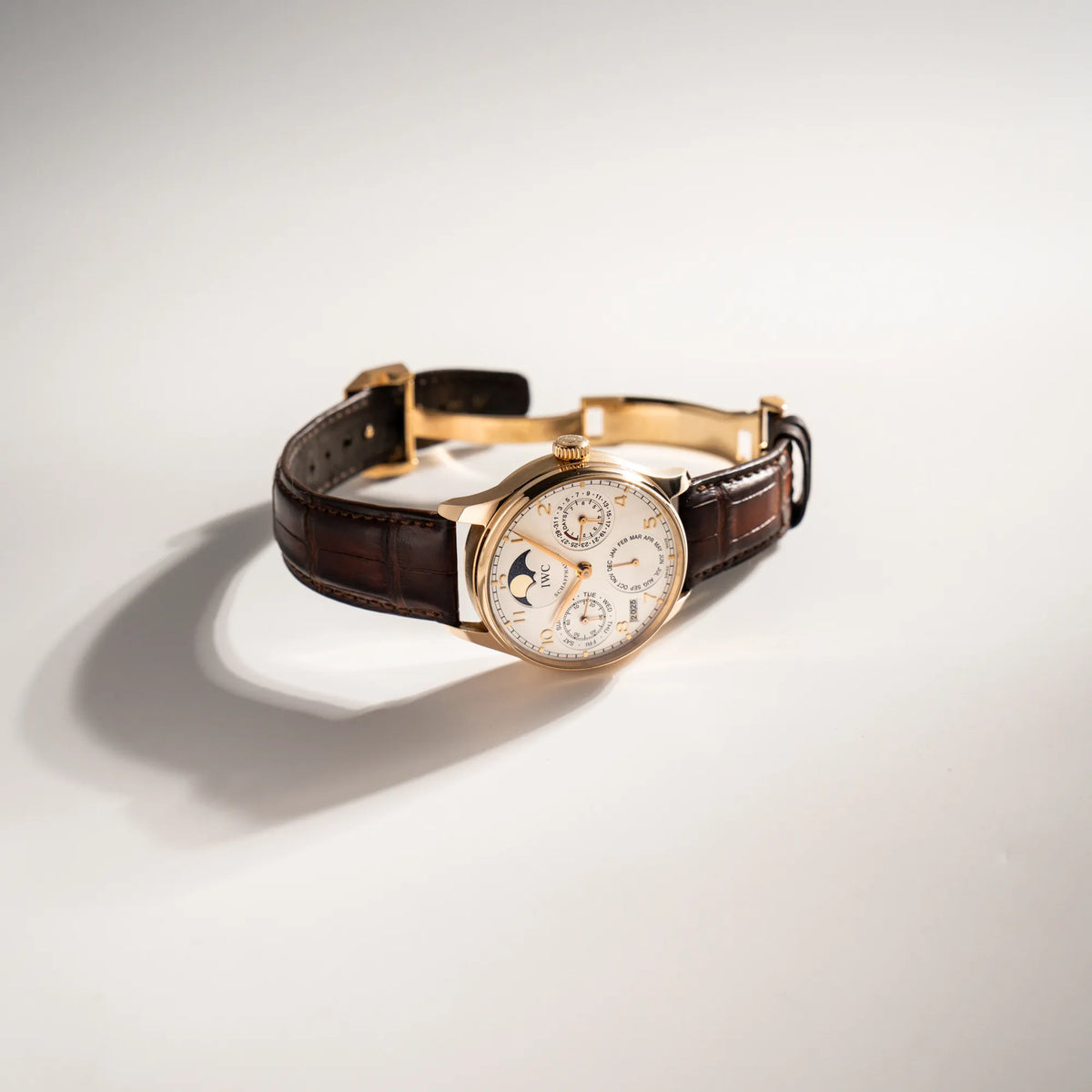 Portugieser Ewiger Kalender IW502213 von IWC in einem 42mm-Rosegold-Gehäuse am braunem IWC Lederband mit einem sanften weißem Zifferblatt liegt seitlich auf dem Uhrengehäuse