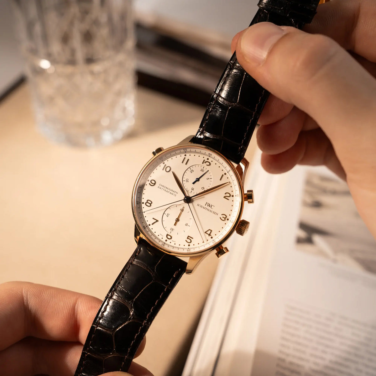 Mann hält den IWC Portugieser Rattrapante Doppel-Chronograph IW3712 aus 18k Roségold mit weißem Zifferblatt am braunen Lederband in den Händen und präsentiert die Armbanduhr in die Kamera