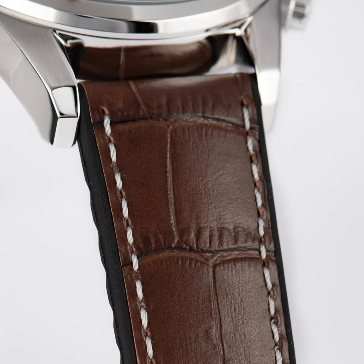 Detailaufnahme des Bandanstoßes der Jacques Lemans 1-2117W Chronograph-Armbanduhr für Herren mit einem anthrazitfarbenen Zifferblatt, roségoldfarbenen Ziegern und Edelstahl-Gehäuse an einem braunem Lederarmband mit einer groben Struktur und mit weißer Ziernaht 