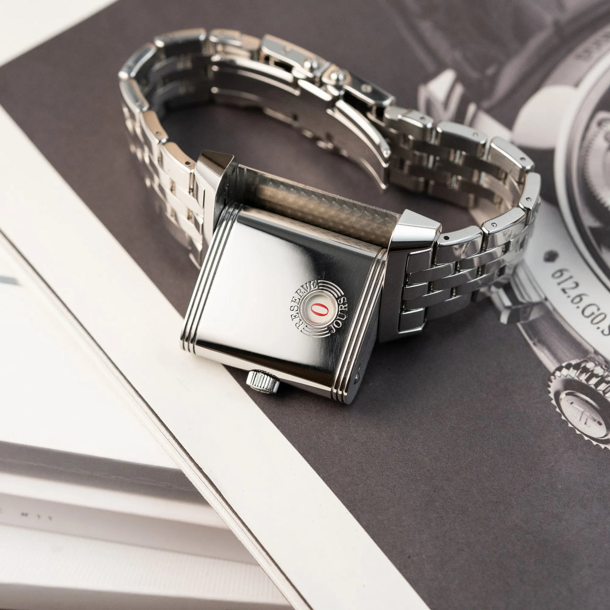 Produktfotografie der Jaeger LeCoultre Grand Reverso 8 am Stahlband mit Blick auf den umgedrehten Gehäuseboden mit der Anzeige der Power-Reserve, während der Reverso-Mechanismus in Funktion ist