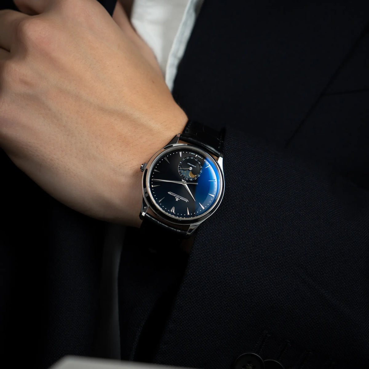 Mann in blauem Sakko trägt die Jaeger-LeCoultre Master Control Q1368470 mit Datum und Mondphase in der schwarzen Zifferblattvariante für einen Wristshot an seinem Handgelenk 