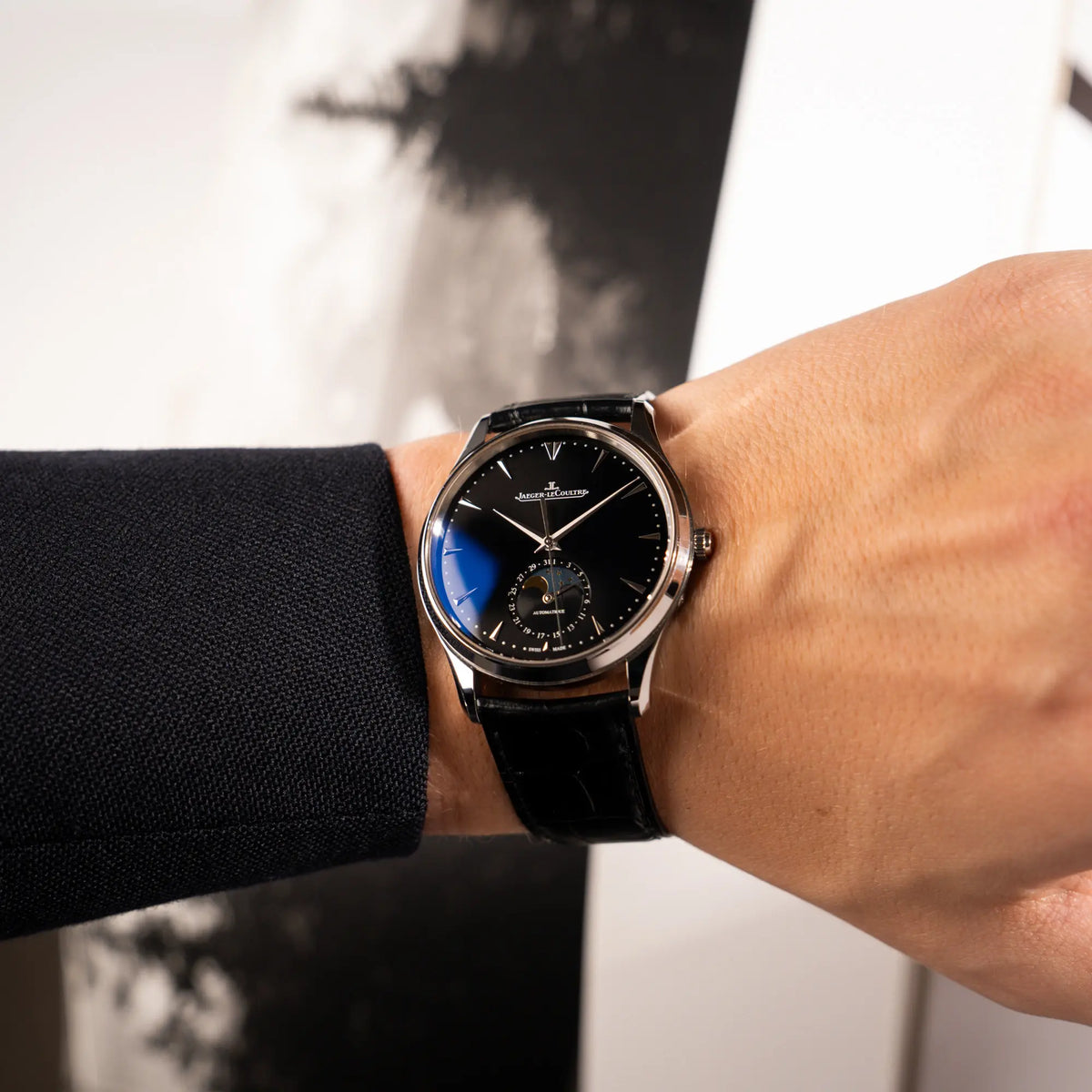 Mann trägt die Jaeger-LeCoultre Master Control Q1368470 mit Datum und Mondphase in der schwarzen Zifferblattvariante an seinem Handgelenk
