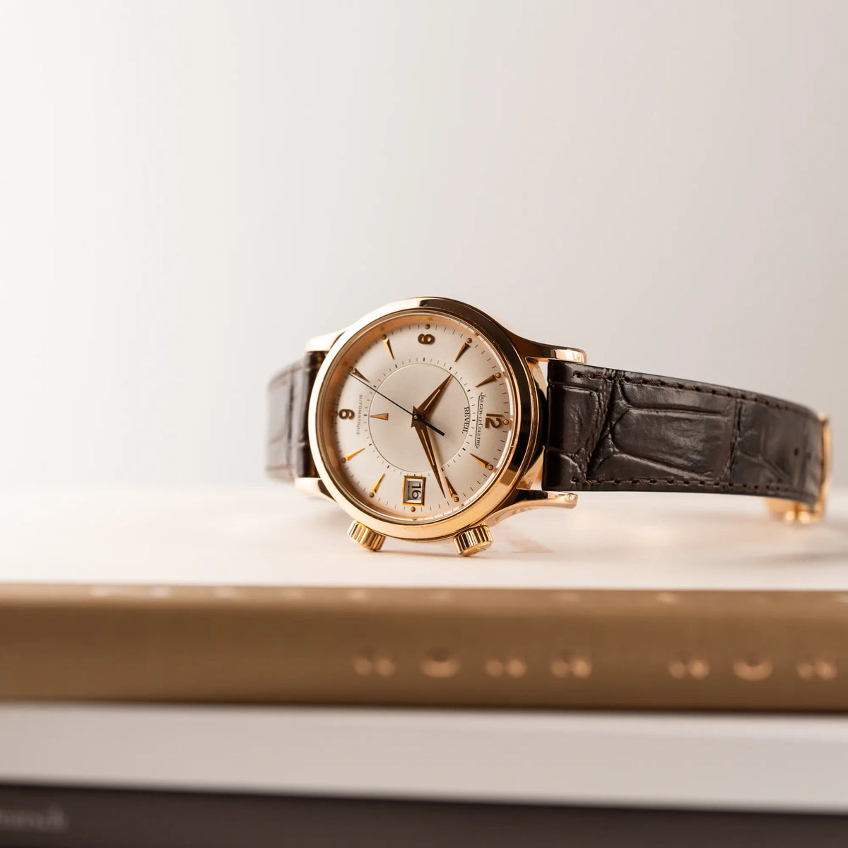 Produktfotografie der auf den zwei Aufzugskronen liegenden Jaeger-LeCoultre Master Memovox 141.2.97 Armbanduhr in Rosegold mit braunem Lederband