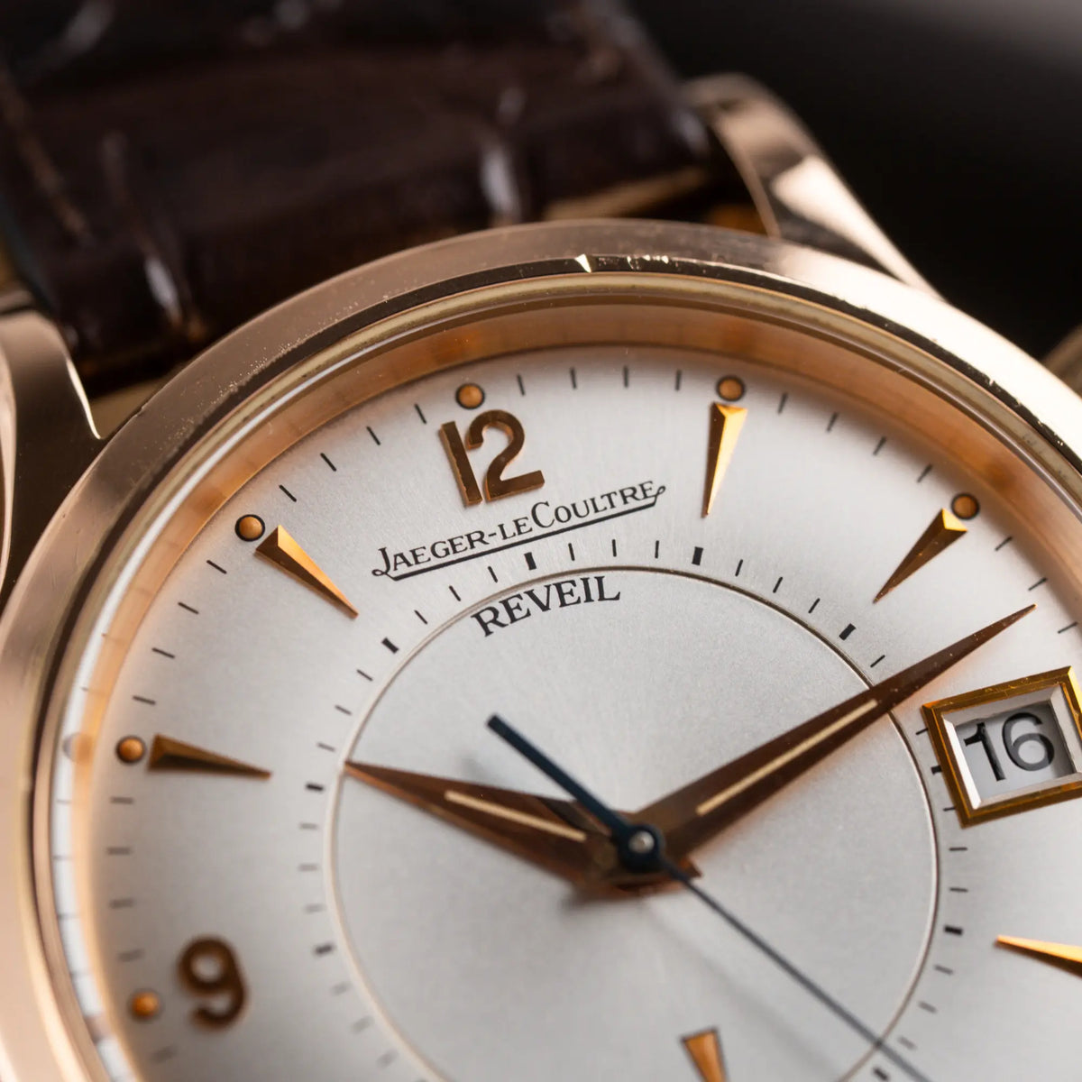 Makroaufnahme der Jaeger-LeCoultre Master Memovox 141.2.97 Armbanduhr in Rosegold am braunem Lederband mit Fokus auf dem Reveil Schriftzug auf dem wei-silbernen Zifferblatt