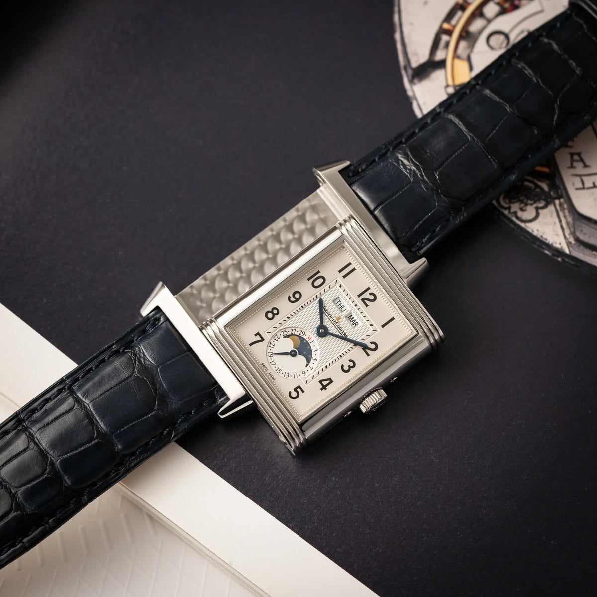 Jaeger-LeCoultre Grande Reverso Calendar 273.8.84 liegt auf einem Buch mit betätigtem Reverso-Mechanismus