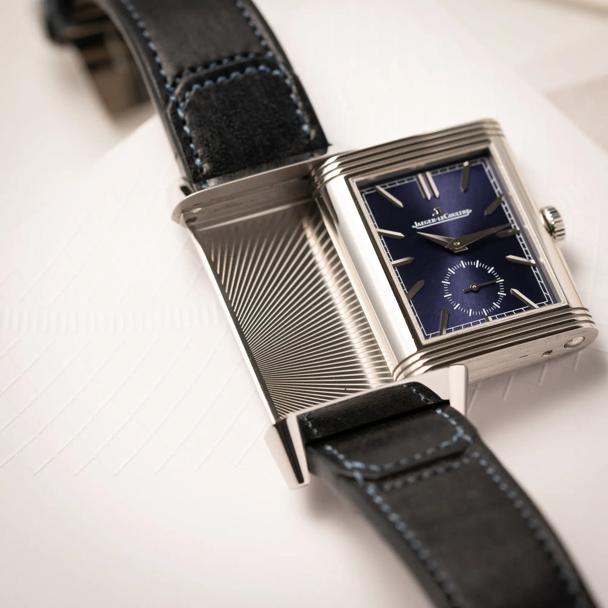 Produktfotografie der Jaeger-LeCoultre Reverso Duoface Q3988482 mit blauem Zifferblatt und weißem Night-and-Day-Zifferblatt am schwarzen Lederband zeigt das blaue Zifferblatt und den betätigten reverso-Mechanismus