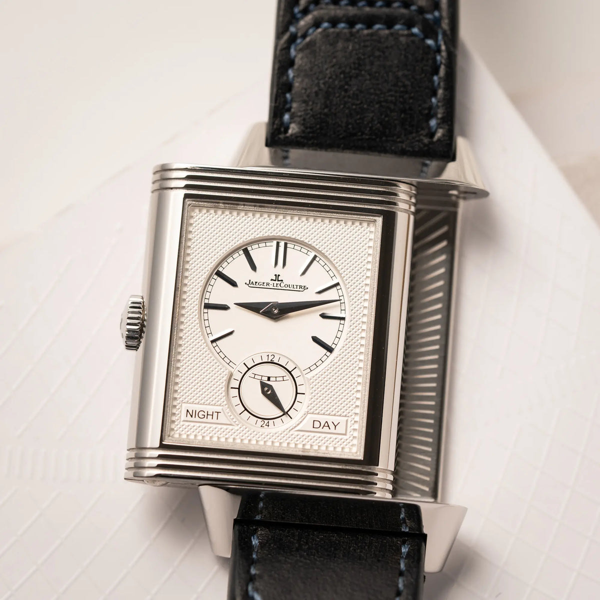 Produktfotografie der Jaeger-LeCoultre Reverso Duoface Q3988482 mit blauem Zifferblatt und weißem Night-and-Day-Zifferblatt am schwarzen Lederband zeigt das weiße guillochierte Zifferblatt und betätigten Reverso-Mechanismus