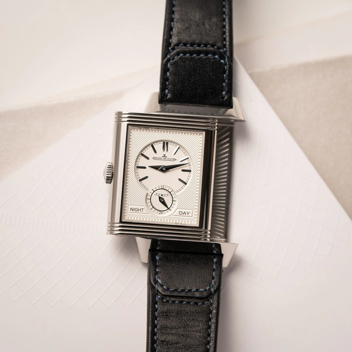 Produktfotografie der Jaeger-LeCoultre Reverso Duoface Q3988482 mit blauem Zifferblatt und weißem Night-and-Day-Zifferblatt am schwarzen Lederband
