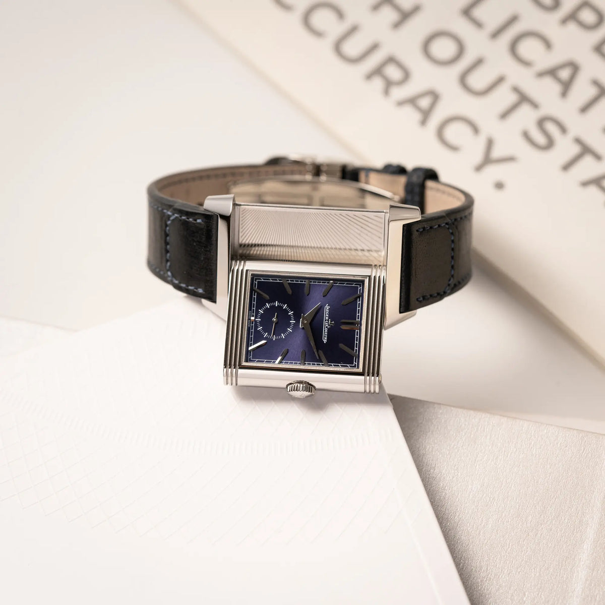 Produktfotografie zeigt die Jaeger-LeCoultre Reverso Duoface Q3988482 mit blauem Zifferblatt und weißem Night-and-Day-Zifferblatt am schwarzen Lederband mit betätigtem Reverso-Mechanismus