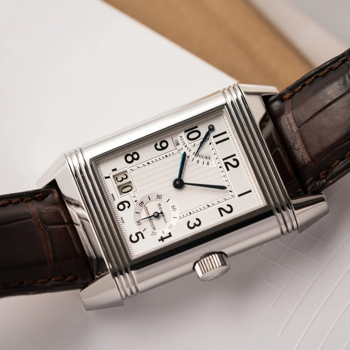 Nahe Produktfotografie der Jaeger-LeCoultre Reverso Grande Date der Referenz 240.8.15 mit silberfarbenem Zifferblatt und Großdatums-Anzeige, kleiner Sekunde und Gangreserve-Anzeige am braunen Lederband