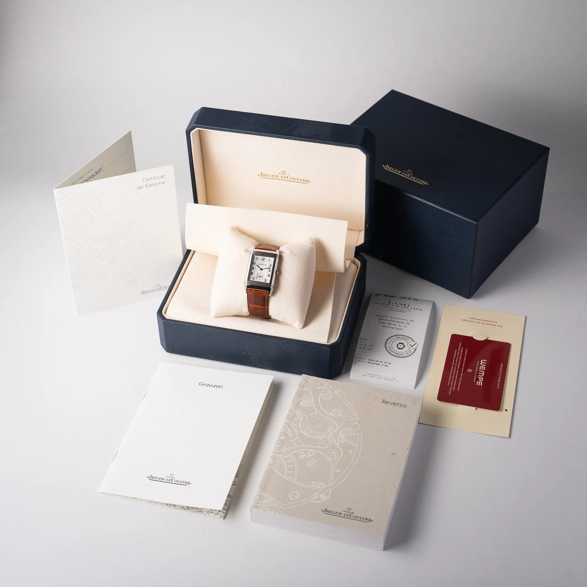 Lieferumfang zu der Jaeger-LeCoultre Reverso Grande Taille der Referenz 270.8.62 mit einem teil-guillochiertem, silberfarbenem Zifferblatt an einem braunem Lederband, betsehend aus Box mit Umkarton, Booklets, Garantieschein, Bedienungsanleitung und Wempe-Garantiekarte