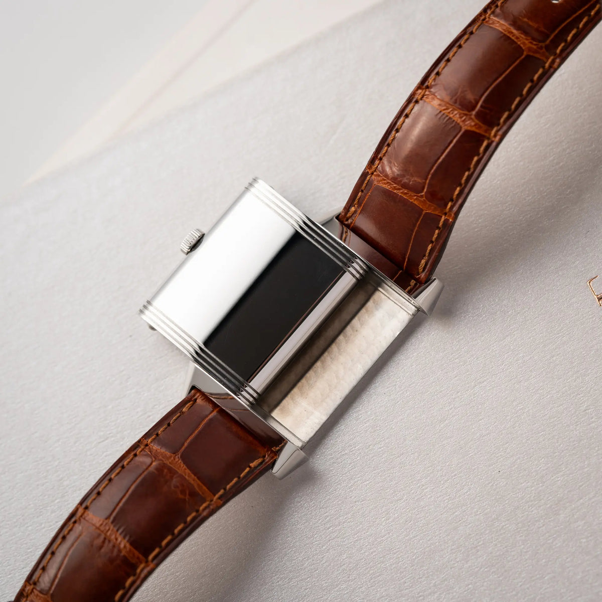 Produktfotografie der Jaeger-LeCoultre Reverso Grande Taille der Referenz 270.8.62 mit einem teil-guillochiertem, silberfarbenem Zifferblatt an einem braunem Lederband zeigt den Gehäuseboden während der Reverso-Mechanismus in Benutzung ist