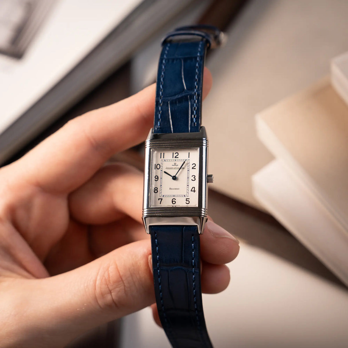 Mann hält die Jaeger-LeCoultre Reverso Classique Medium 250.8.86 in Edelstahl an einem dunkelblauem Lederband in seiner Hand und präsentiert die Uhr in die Kamera