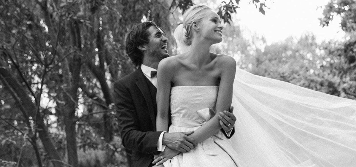 Schwarz weiße Fotografie eines Brautpaars an Ihrem Hochzeitstag wo der Bräutigam die Braut von hinten umarmt