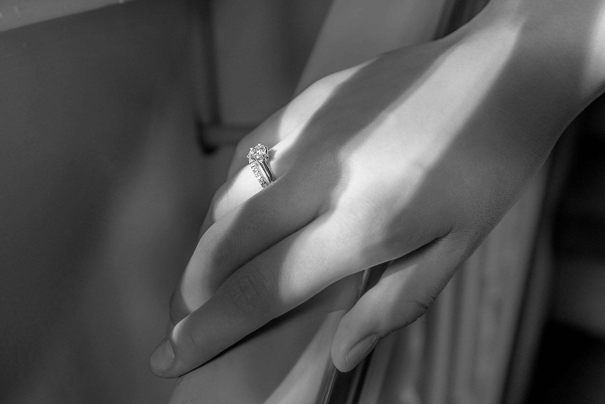 Schwarz weiße Fotografie der Hand einer Dame mit Verlobungsring und Ehering an ihrem Ringfinger