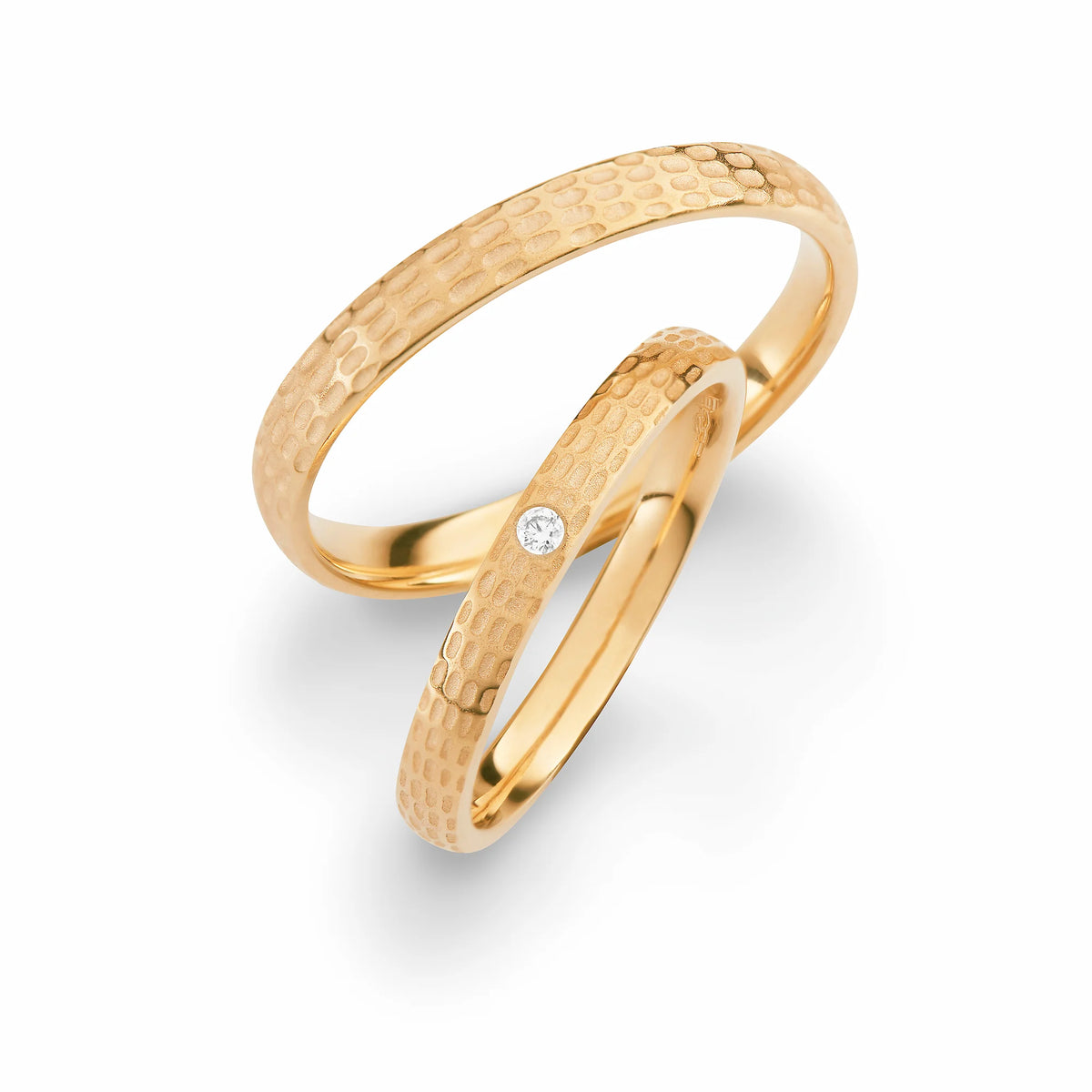 Produktfotografie des gelbgoldenen Max Kemper Trauringpaars mit einzigartiger Oberflächenstruktur bestehend aus kleinen Gravurflächen und mit einem Diamant als Highlight für den Damenring