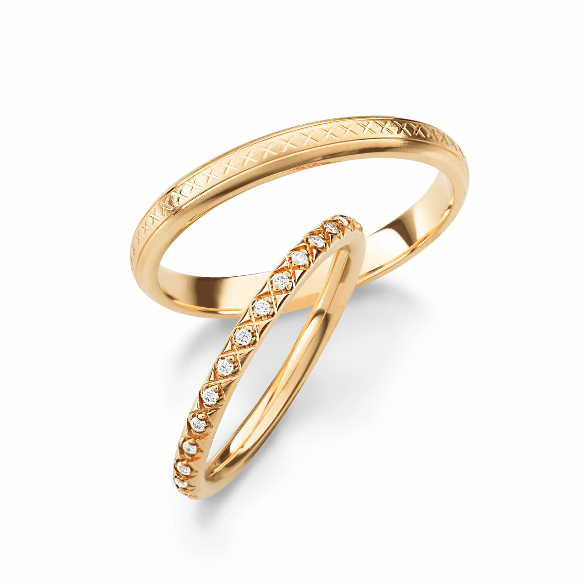 Produktfotografie des gelbgoldenen Max Kemper Trauringpaars mit einer feinen Oberflächenstruktur und sich wiederholenden, eingravierten X-Designs und Diamanten im Damenring, die in das X-Design eingefasst wurden