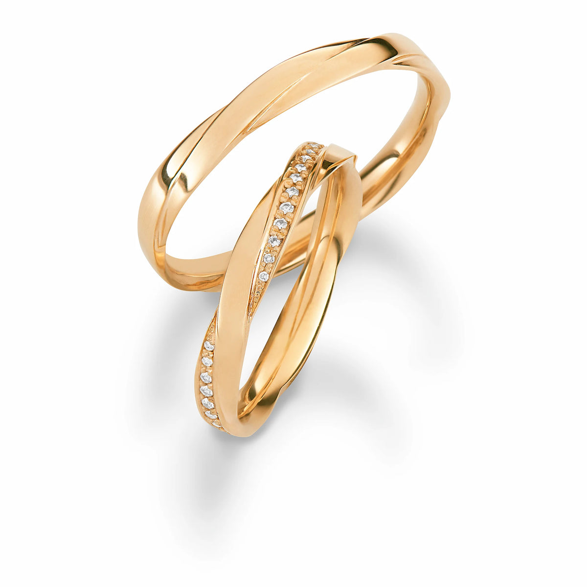 Produktfotografie des gelbgoldenen Max Kemper Trauringpaars mit einer einzigartigen Form derfümmen Ringschiene, die an zwei ineinander verschmelzende Ringe erinnert, mit einer polierten Oberfläche  und speziell für den Damenring eingefassten Diamant-Schienen