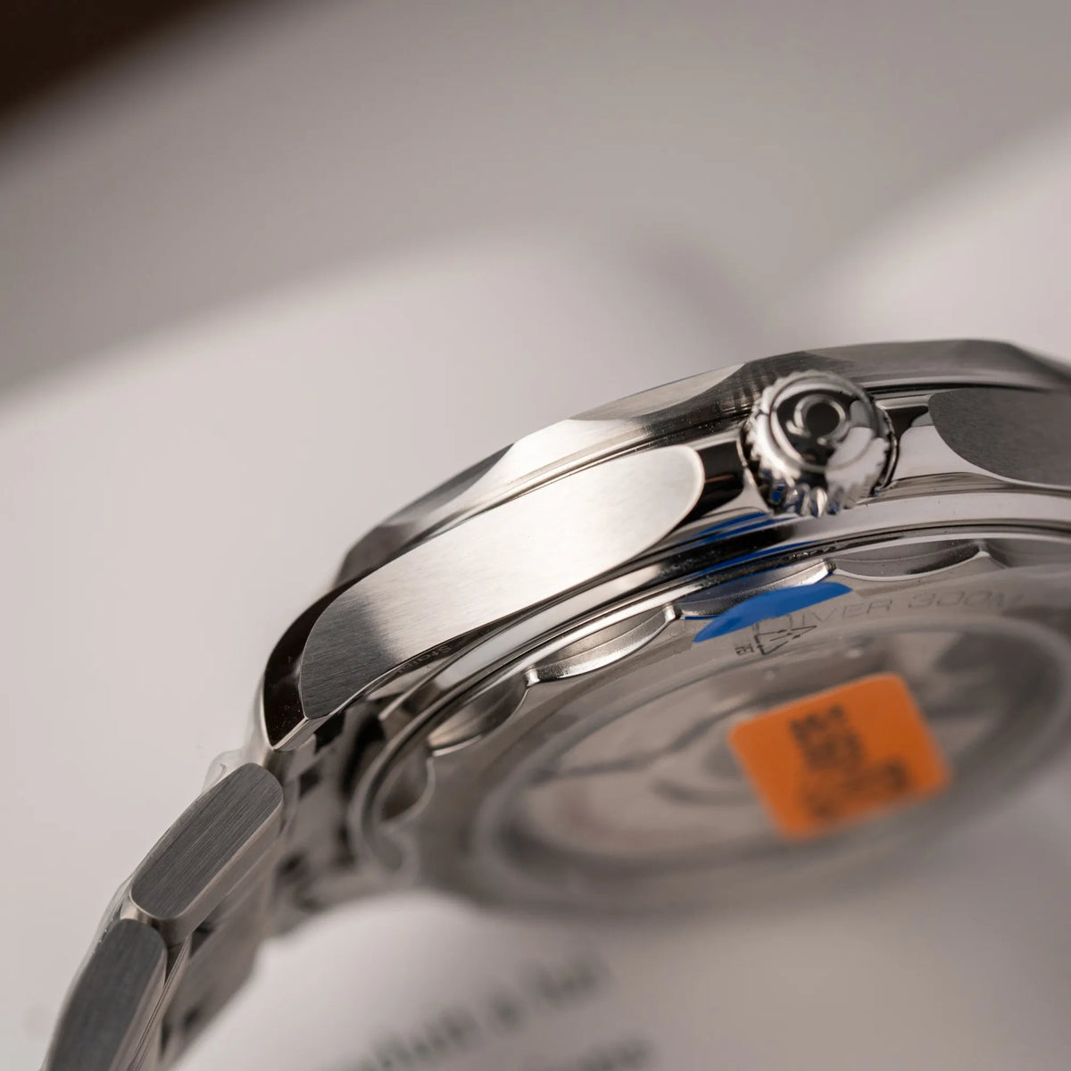 Detailaufnahme der seitlichen Gehäuseflanke der Omega Seamaster Diver 300M der Referenz 210.30.42.20.06.001 mit grauem Zifferblatt im Wellen-Design und blauer Lünette am Edelstahlarmband, welches zum Schutz verklebt wurde
