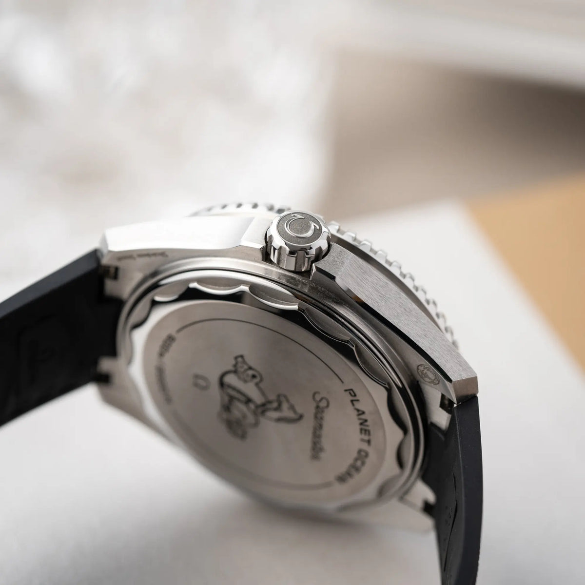 Produktfotografie zeigt die Aufzugskrone im Fokus von der Omega Seamaster Planet Ocean der Referenz 217.32.42.21.01.001 (4. Generation) mit schwarzem Zifferblatt und Lünette am schwarzen Kautschuk-Armband