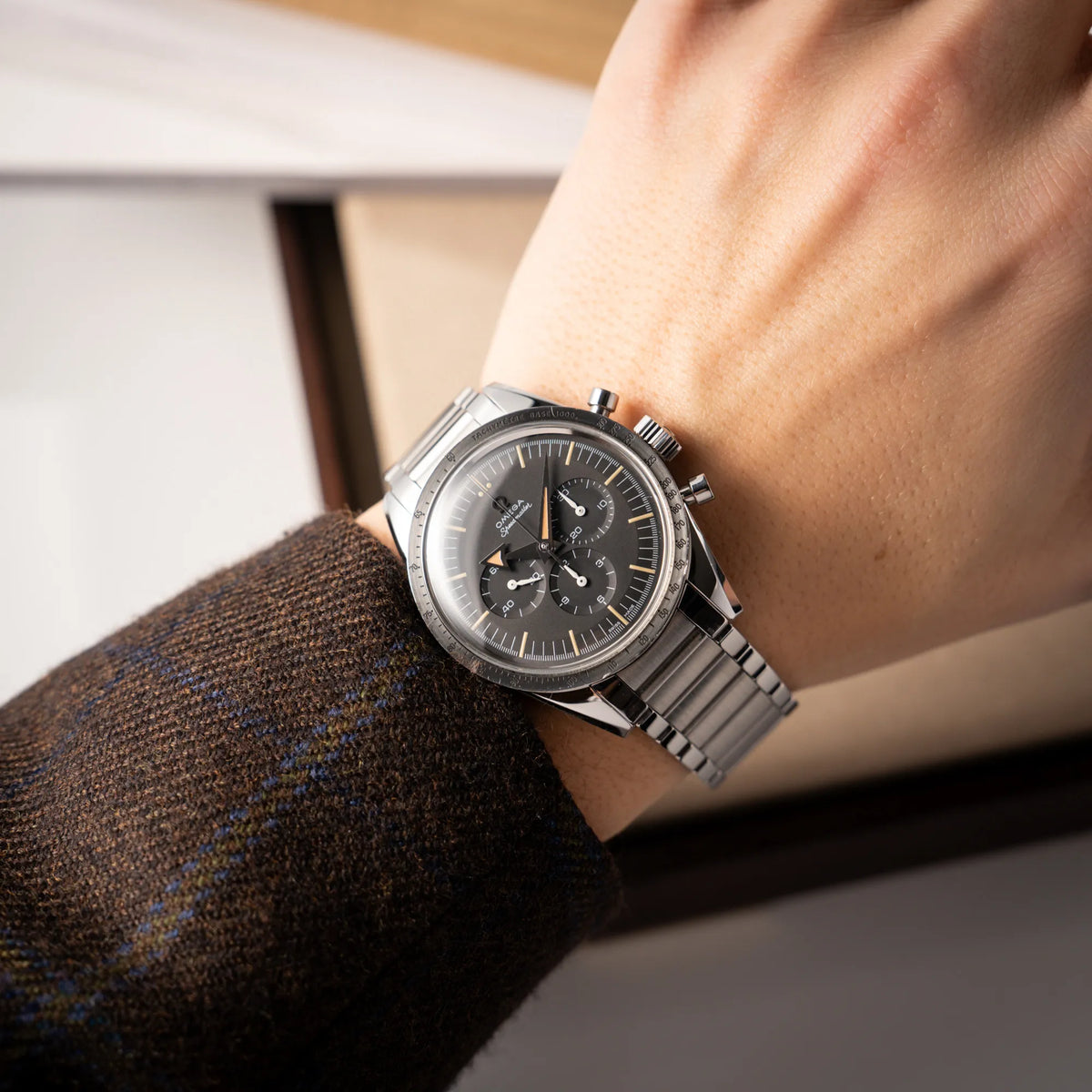 Mann in braunem Sakko trägt die Omega Speedmaster 1957 Trilogy Limited Edition mit einem anthrazitfarbenen Zifferblatt mit Vintage-Look und dem original Omega-Stahlband im Ed-White-Design an seinem Arm