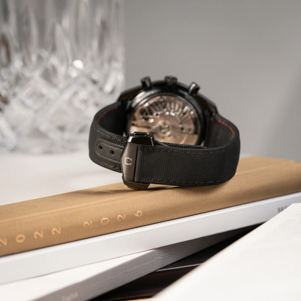Produktfotografie von dem Omega Speedmaster "Darkside of the Moon" Chronograph mit schwarzem Zifferblatt und aus schwarzer Keramik gefertigtem Gehäuse mit Blick auf das Textil-Armband und die schwarze Faltschliesse