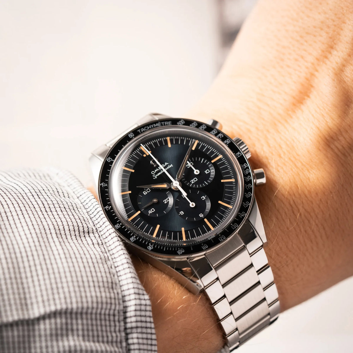 Mann trägt die Omega Speedmaster FOIS der Referenz 310.30.40.50.06.001 mit dem dunkelblauen Zifferblatt mit dunkel-beigen Indizes im Vintage-Look und einem vom Standard-Modell abgeänderten Stahl-Armband, was beides an das klassische Speedy-Modell erinnert, für einen Wristshot an seinem Handgelenk