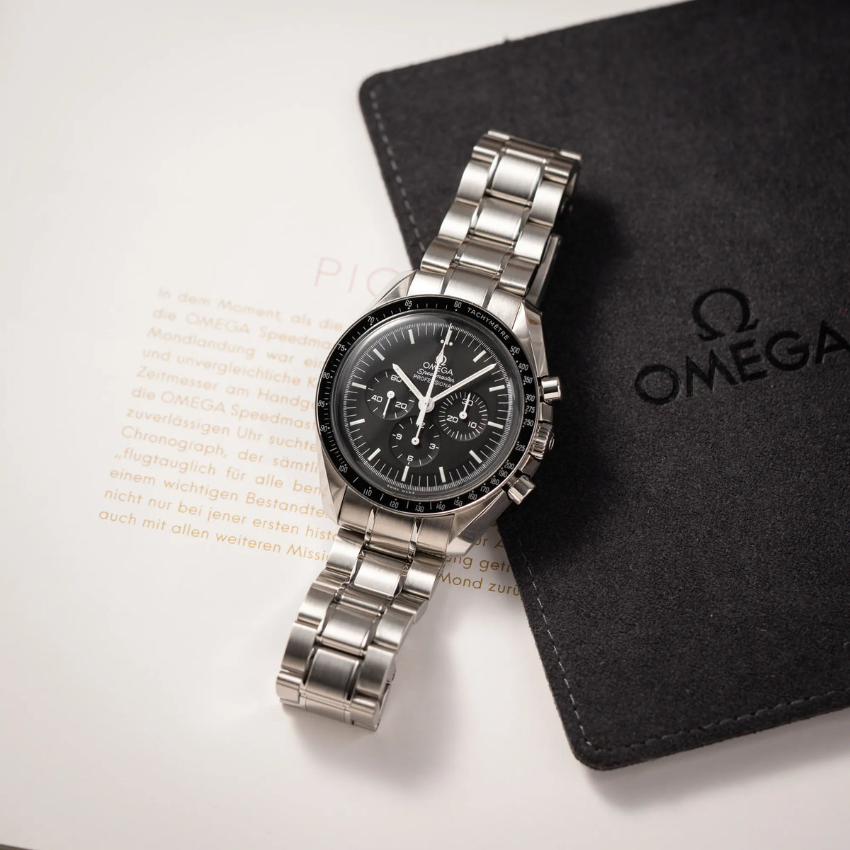 Produktfotografie der auf dem Band liegenden Omega Speedmaster Professional Moonwatch der Referenz 311.30.42.30.01.005 in einem 42mm-Gehäuse mit klassischem schwarzen Zifferblatt und verbautem Hesalitglas